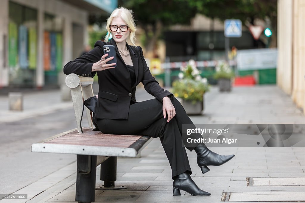 Albino executive sitting on a city bench while looking at her Smart Phone
