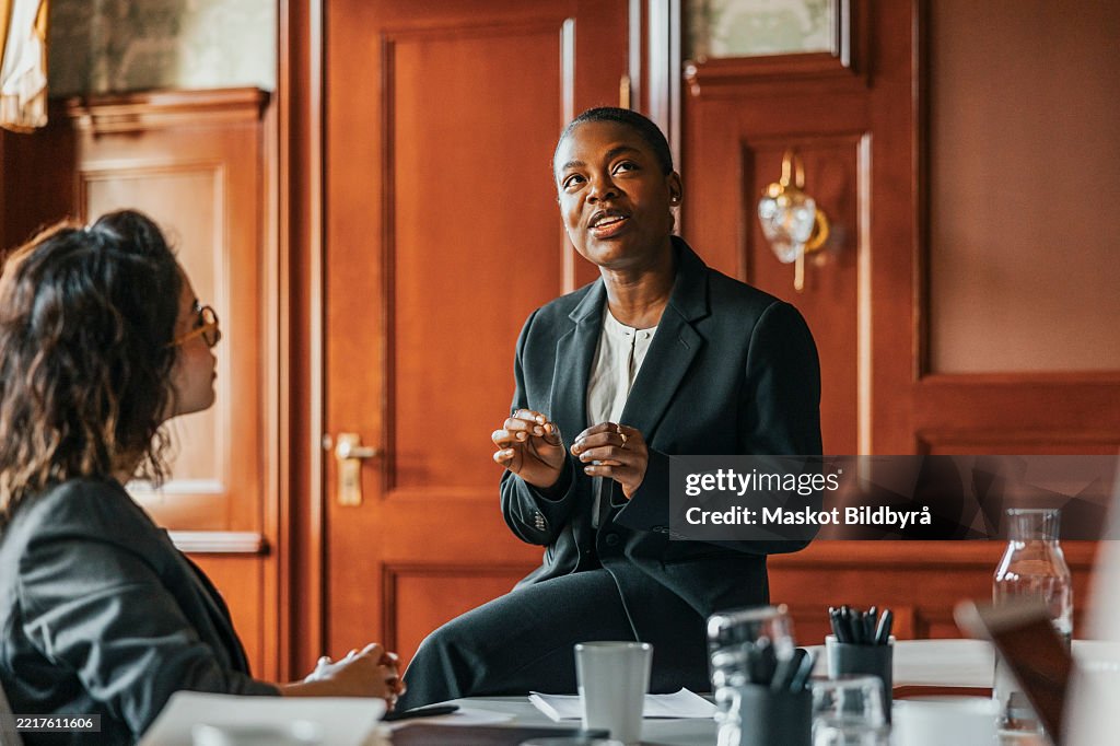 Businesswoman talking with female colleague while sitting on table in meeting room