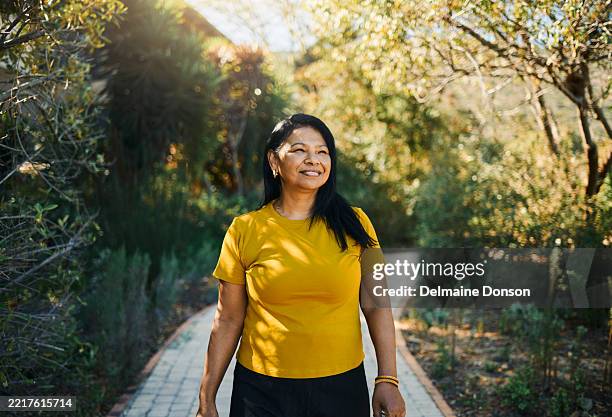 smiling woman strolling through sunny garden path - mature indian woman portrait stock pictures, royalty-free photos & images