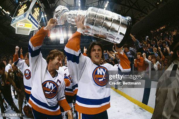 The New York Islanders' Denis Potvin and Mike Bossy raise the Stanley Cup trophy aloft as they celebrate with teammates at the Nassau Veterans...