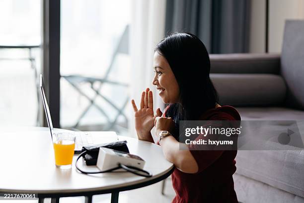 asian malay woman taking blood pressure at home while having online meeting with a doctor - health monitoring stock pictures, royalty-free photos & images