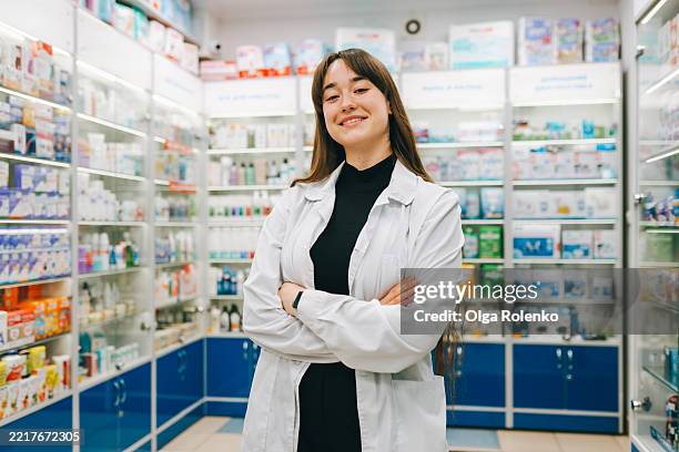 young pharmacist smiling with crossed arms in a pharmacy - knowledge is power stock pictures, royalty-free photos & images