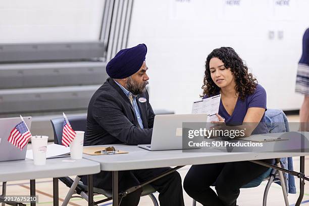 poll workers assisting voter with laptop and documents - polling place stock pictures, royalty-free photos & images
