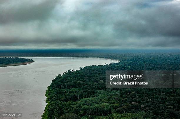 Aerial view of the Madeira River on a stormy day, captures the river's sweeping meanders and surrounding dense rainforest, with visible patches of...