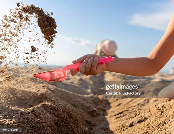 bambini che giocano sulla spiaggia con pale giocattolo sotto un cielo soleggiato - scavare foto e immagini stock