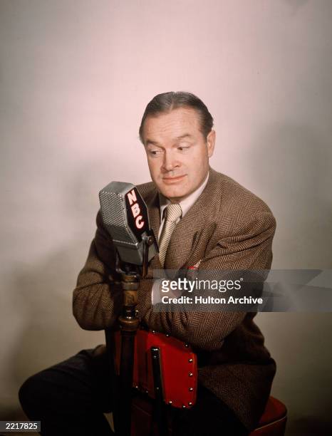 Promotional studio portrait of British-born comedian and actor Bob Hope sitting at an NBC radio microphone, 1940s.