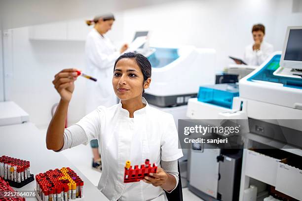 junger medizinischer forscher, der blutproben in einem modernen klinischen labor mit weißer uniform untersucht - nanomedizin stock-fotos und bilder