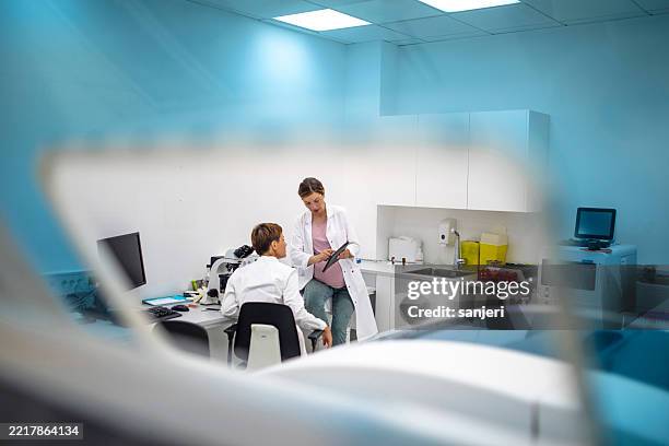 laborwissenschaftlerinnen in weißen kitteln beraten über forschungsdaten, schwangere forscherin bei der arbeit - nanomedizin stock-fotos und bilder