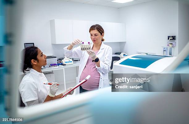 schwangere laborwissenschaftlerin und indische kollegin untersuchen testproben in einem modernen medizinischen labor - nanomedizin stock-fotos und bilder