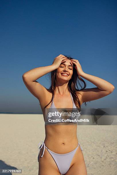 mujer joven sonriendo en una playa soleada con cielo azul vibrante - biquini fotografías e imágenes de stock