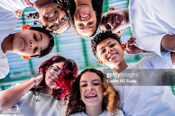 portrait of student friends huddling on the sports court at school - schooljongen stockfoto's en -beelden