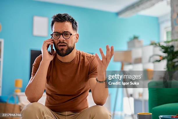 joven frustrado discutiendo por teléfono en casa - quejándose fotografías e imágenes de stock