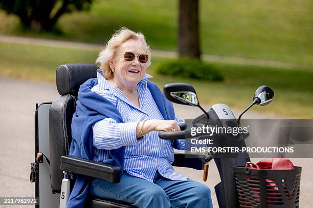 active happy senior woman in her 80ies with physical disabilities drives with an electric mobility scooter and explores the city park quite cheerful. - veicolo elettrico automobile con biodiesel foto e immagini stock