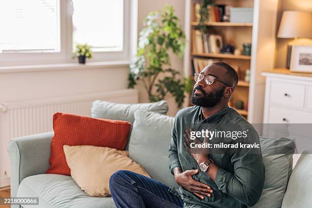 serene man practicing mindfulness on sofa at home - hands on chest stock pictures, royalty-free photos & images