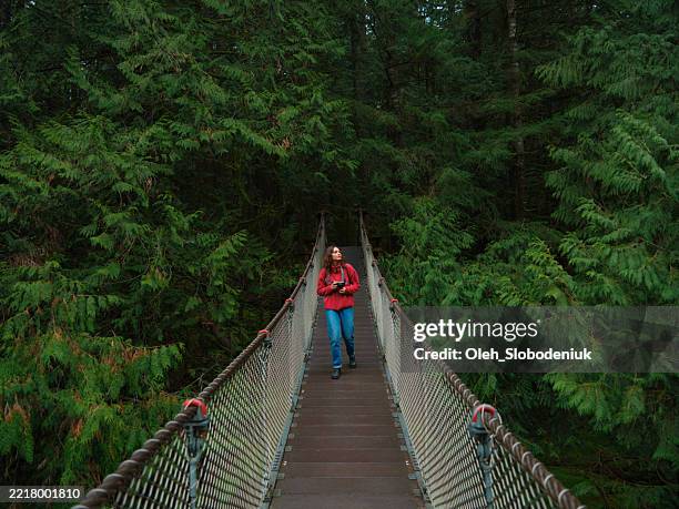 frau geht auf der lynn canyon hängebrücke in vancouver, kanada - hängebrücke stock-fotos und bilder