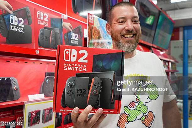 French customer living in Tokyo smiles as he shows off a Nintendo Switch 2 bought at an electronics retailer in Tokyo on June 5, 2025. With shops...