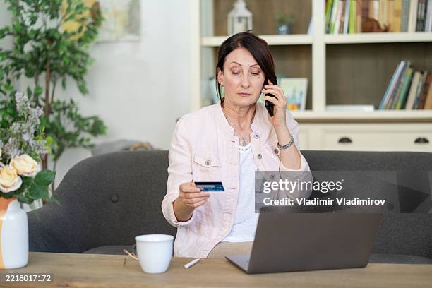 woman at home on a call while holding a credit card. - scam victim stock pictures, royalty-free photos & images