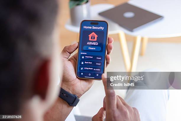 hombre armando el sistema de seguridad del hogar usando la aplicación móvil - alarma de seguridad fotografías e imágenes de stock