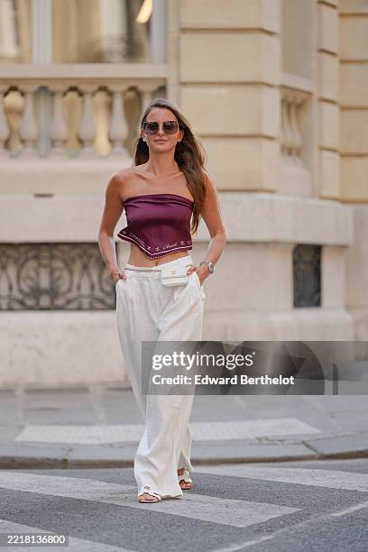 Diane Batoukina wears a strapless crop top from Chanel in a deep burgundy color with a subtle sheen, featuring a printed border along the hem. The...