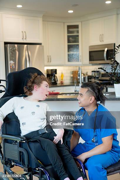 caregiver assisting young woman in wheelchair in home environment - assistive technology stock pictures, royalty-free photos & images