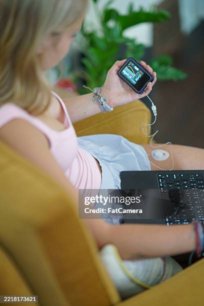 woman using a glucometer device while working on a laptop at home - homeostasis stock pictures, royalty-free photos & images