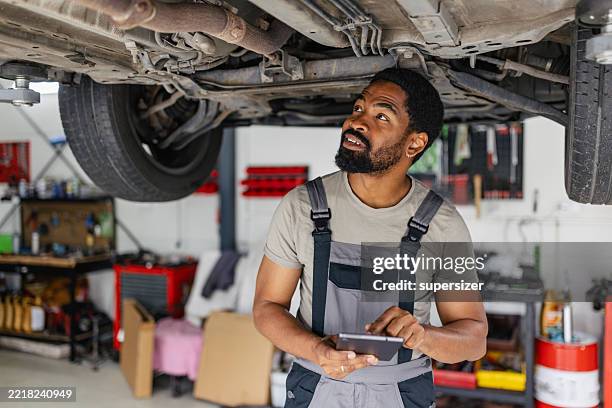 mechanic working underneath a vehicle in garage - undercarriage stock pictures, royalty-free photos & images