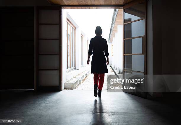 woman alone leaving the dark room and walking to bright corridor - woman walking out door silhouette stock pictures, royalty-free photos & images