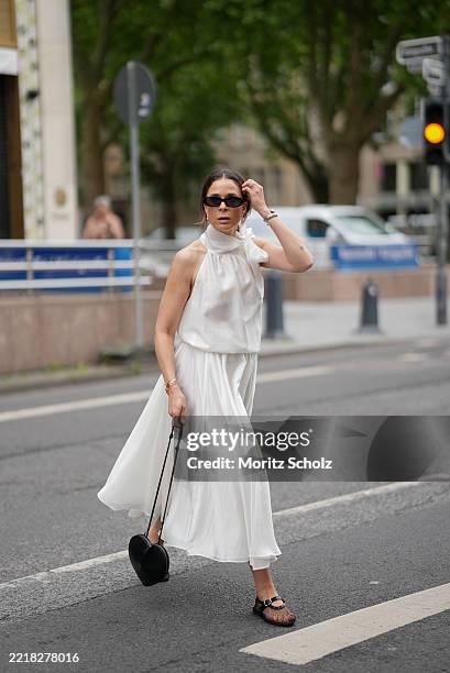 Patricia Wirschke is seen wearing a white two-piece consisting of a flowy midi skirt and a sleeveless blouse with high collar and tie detail at the...