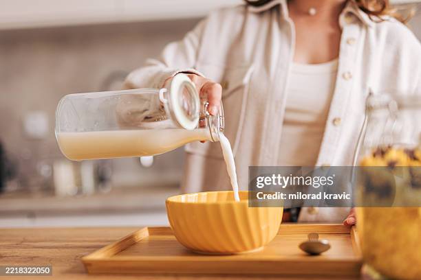 frau gießt hafermilch in eine schüssel für frühstücksflocken in der küche - hafermilch stock-fotos und bilder