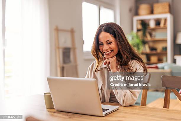 mujer joven que trabaja desde casa y sonríe a la computadora portátil - observar fotografías e imágenes de stock