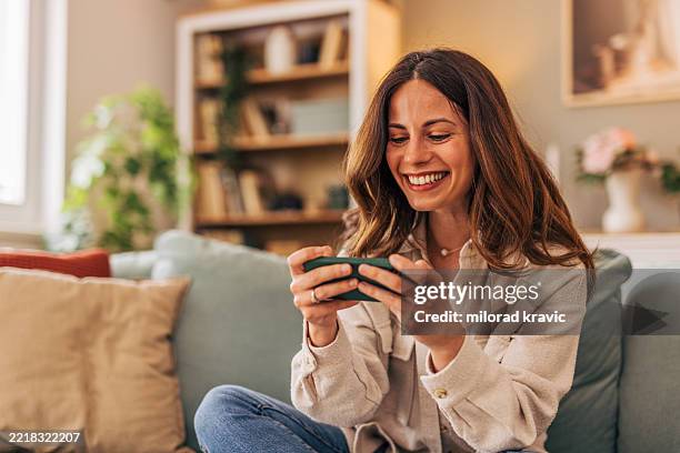 femme heureuse jouant à des jeux mobiles sur smartphone à la maison - jeu mobile photos et images de collection