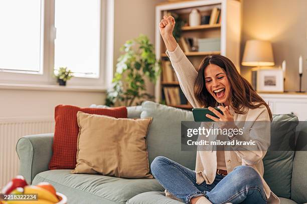 aufgeregte frau, die erfolg auf dem smartphone zu hause feiert - gewinnen stock-fotos und bilder