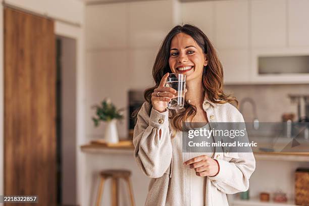 junge frau, die wasser in moderner küche trinkt, lächelt in die kamera - wasser trinken stock-fotos und bilder