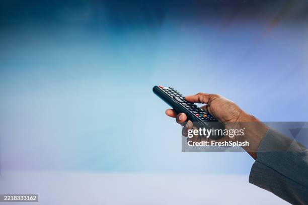 hand holding remote control against a colorful gradient background - remote control stock pictures, royalty-free photos & images