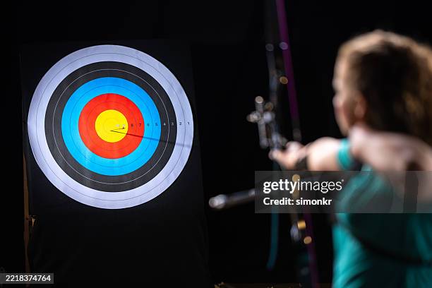 female archer hits bullseye with recurve bow in studio - professional bow stock pictures, royalty-free photos & images
