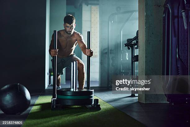 determined athletic man having sled training in a gym. - sled push stock pictures, royalty-free photos & images