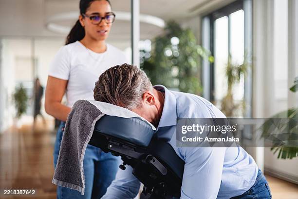 mid adult businessman getting office massage from young female therapist in modern workspace - massaging stock pictures, royalty-free photos & images