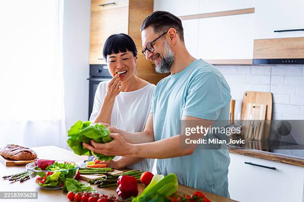 socios felices preparando ensalada en una cocina moderna - comida sana fotografías e imágenes de stock