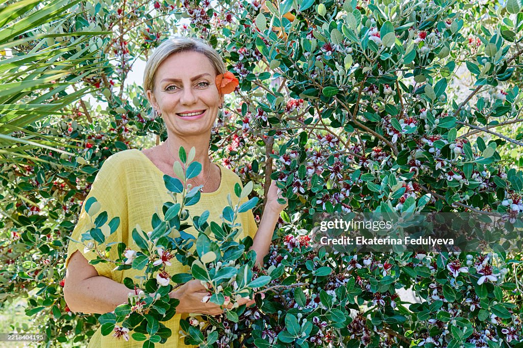 Portrait of mature smiling blond woman near Feijoa sellowiana or Acca sellowiana in bloom