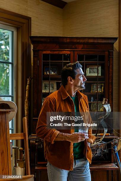 successful man holding a whiskey glass while looking away at home - warmes licht stock-fotos und bilder