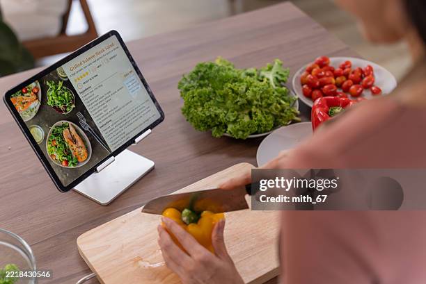 asian woman preparing salad while following healthy recipe on tablet screen - cookbook stock pictures, royalty-free photos & images