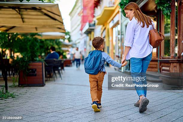 mutter und sohn gehen hand in hand auf einer straße in der stadt - gemeinsam gehen stock-fotos und bilder