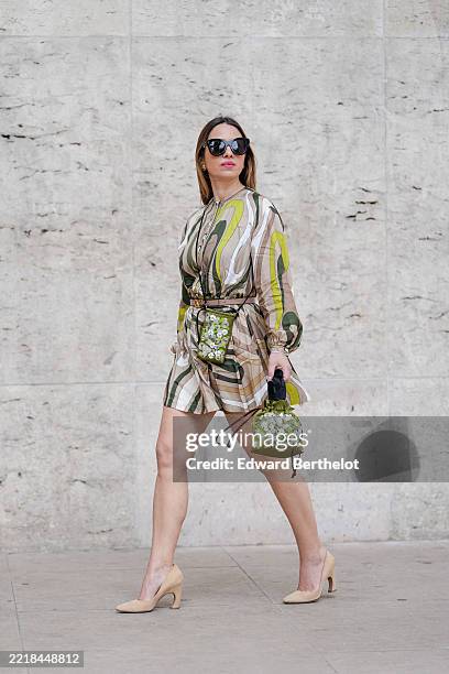 Maria Rosaria Rizzo wears oversized black sunglasses and gold hoop earrings. The hair is styled straight and loose. The dress features a multicolored...