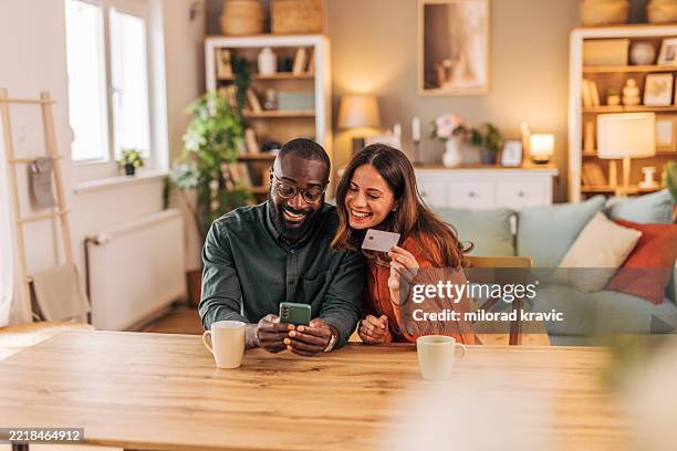 happy couple making online payment using credit card and smartphone at home - handing over credit card stock pictures, royalty-free photos & images