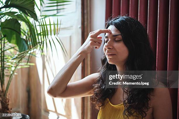 calm peaceful young woman sitting in lotus pose practicing eft tapping to relieve stress, touching forehead with fingertips. emotional freedom technique - pressure point stock pictures, royalty-free photos & images