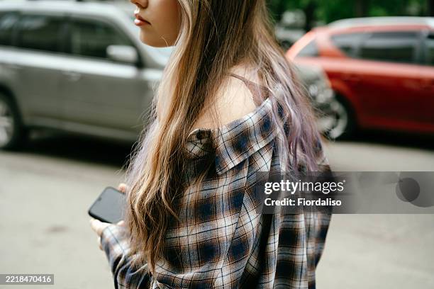 fashionable young woman holding smartphone outdoors in urban setting - checked shirt stock pictures, royalty-free photos & images