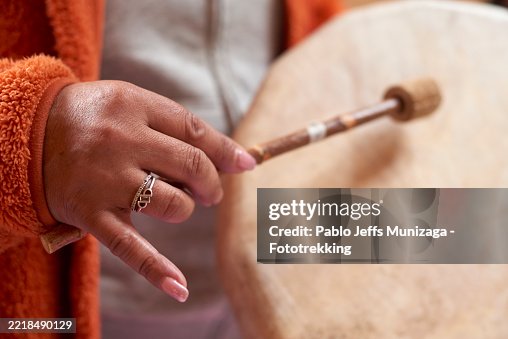 Close-up of a woman's hand gently holding a drumstick, poised to strike a large native drum during a therapeutic session, invoking mindfulness and healing Close-up of a woman's hand gently holding a drumstick, poised to strike a large native drum during a therapeutic session, invoking mindfulness and healing