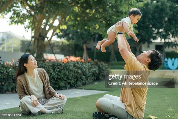 proud young father lifting his baby high into the sky, laughing and smiling while building trust, connection, and core memories - mexer imagens e fotografias de stock