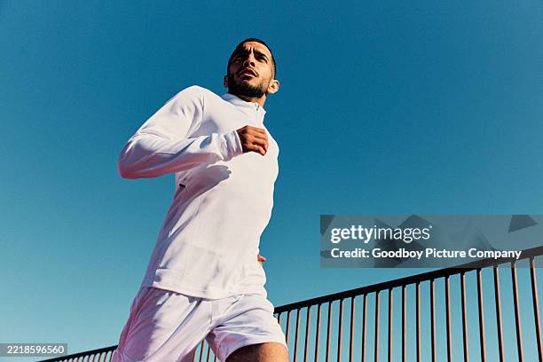 junger mann in weißer sportbekleidung, der bei strahlend blauem himmel im freien läuft und wegschaut - rennen stock-fotos und bilder