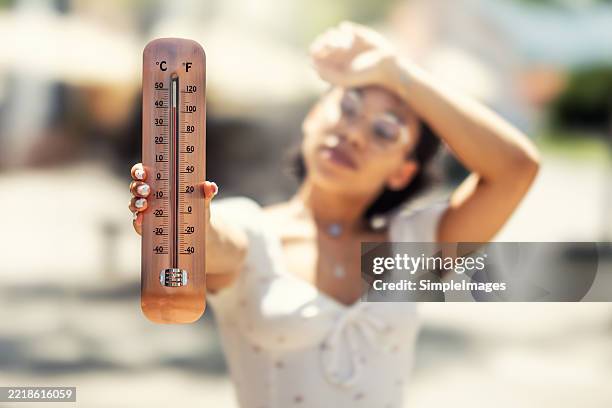 a thermometer showing high temperatures is held by a young woman somewhere in the city streets - temperatura imagens e fotografias de stock